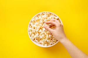 hand going into a tub of popcorn with yellow background