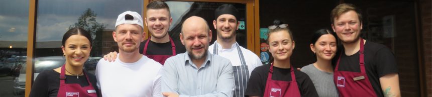 staff members pose for photo outside restaurant entrance to celebrate trip advisor certificate of excellence