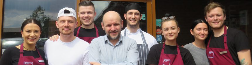 staff members pose for photo outside restaurant entrance to celebrate trip advisor certificate of excellence