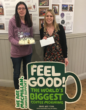 bake off competition winner gemma stands with cake and macmillan poster